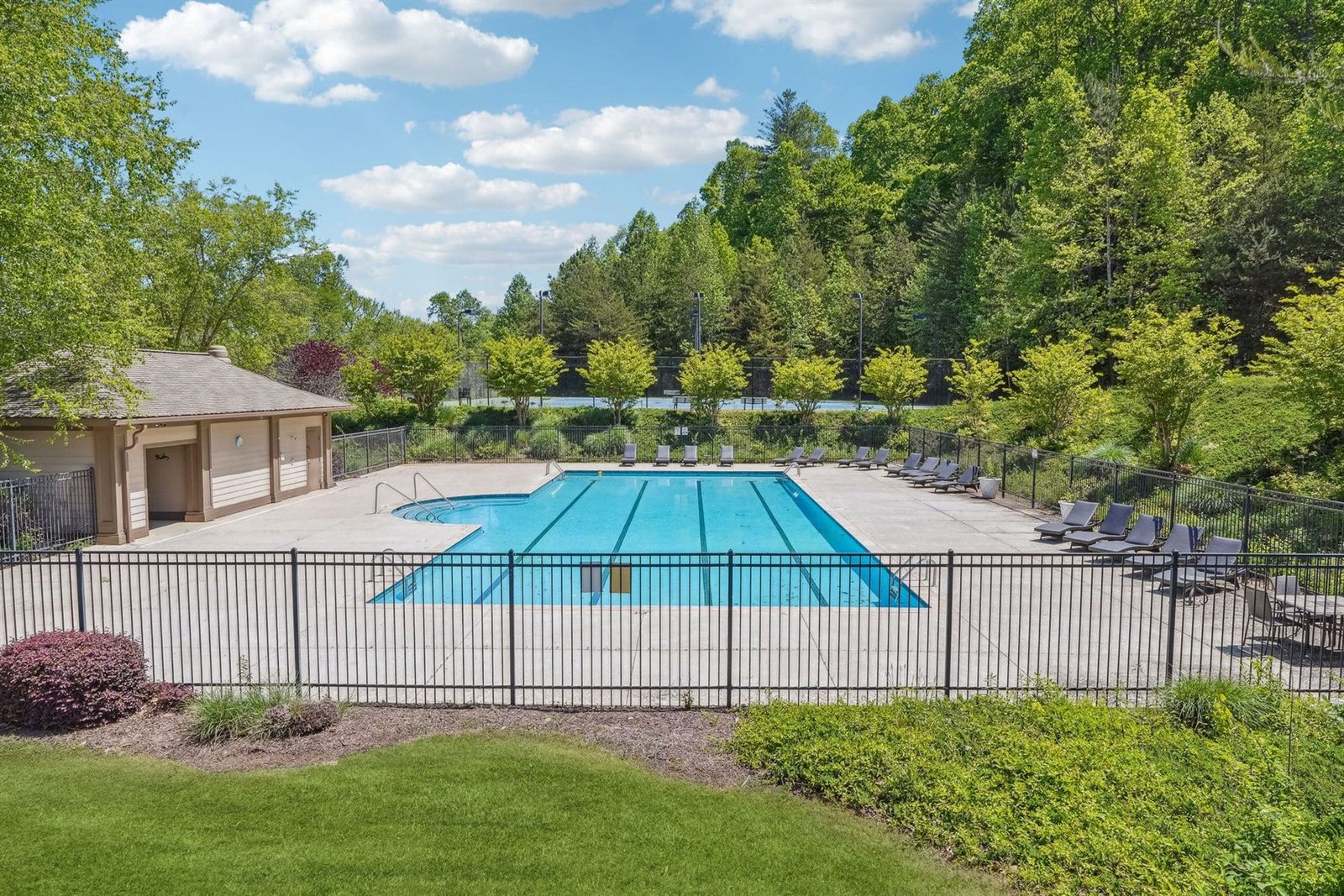 The Achasta community swimming pool &mdash; resort-style rectangular pool with stone-and-paver deck, lounge seating, an adjacent pool house and a wooded backdrop &mdash; one of the Achasta private community amenities in Dahlonega, Georgia