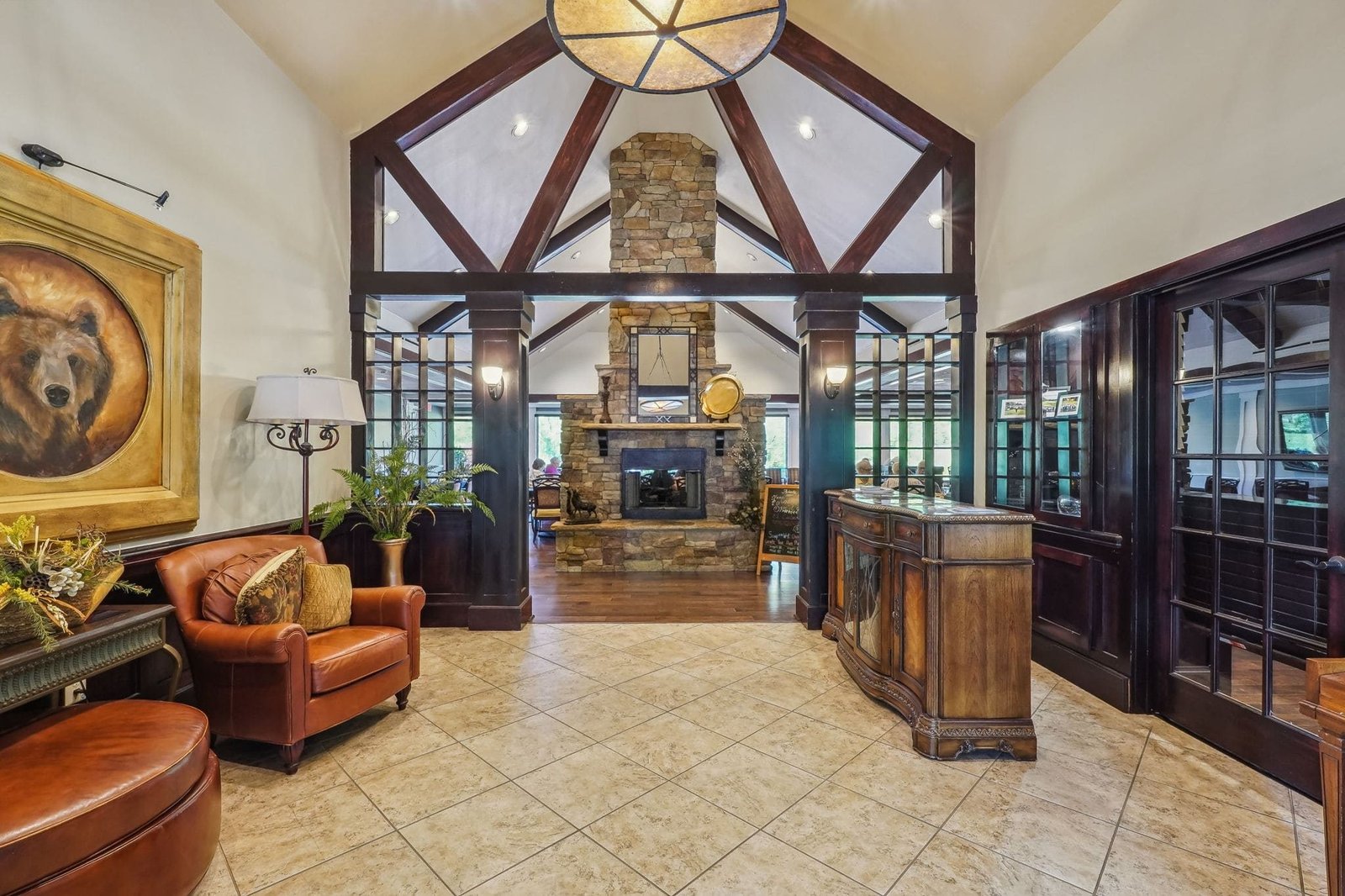 Achasta clubhouse great room interior &mdash; vaulted timber-and-stone room, fireplace, leather seating arrangements, large windows looking onto the golf course