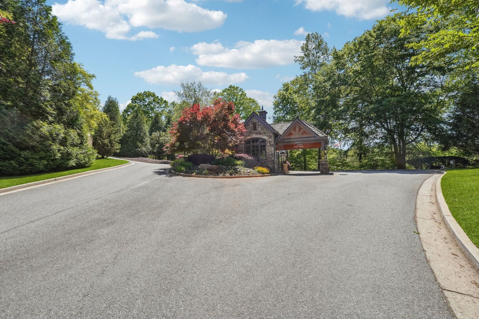 The primary stone-and-timber gatehouse at Achasta in Dahlonega Georgia &mdash; staffed entry, wide paved sweep, mature hardwoods on either side of the access drive off Long Branch Road